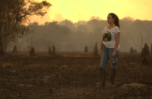 Manoela Machado stands among burned vegetation in a smoky sunset