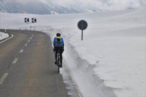 A cyclist rides on a plowed road with snow on either side