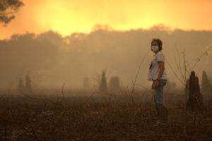 A researcher wearing a mask stands in a smoky, orange-lit landscape