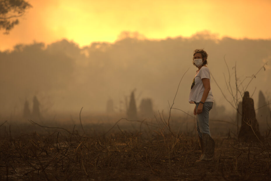 A researcher wearing a mask stands in a smoky, orange-lit landscape