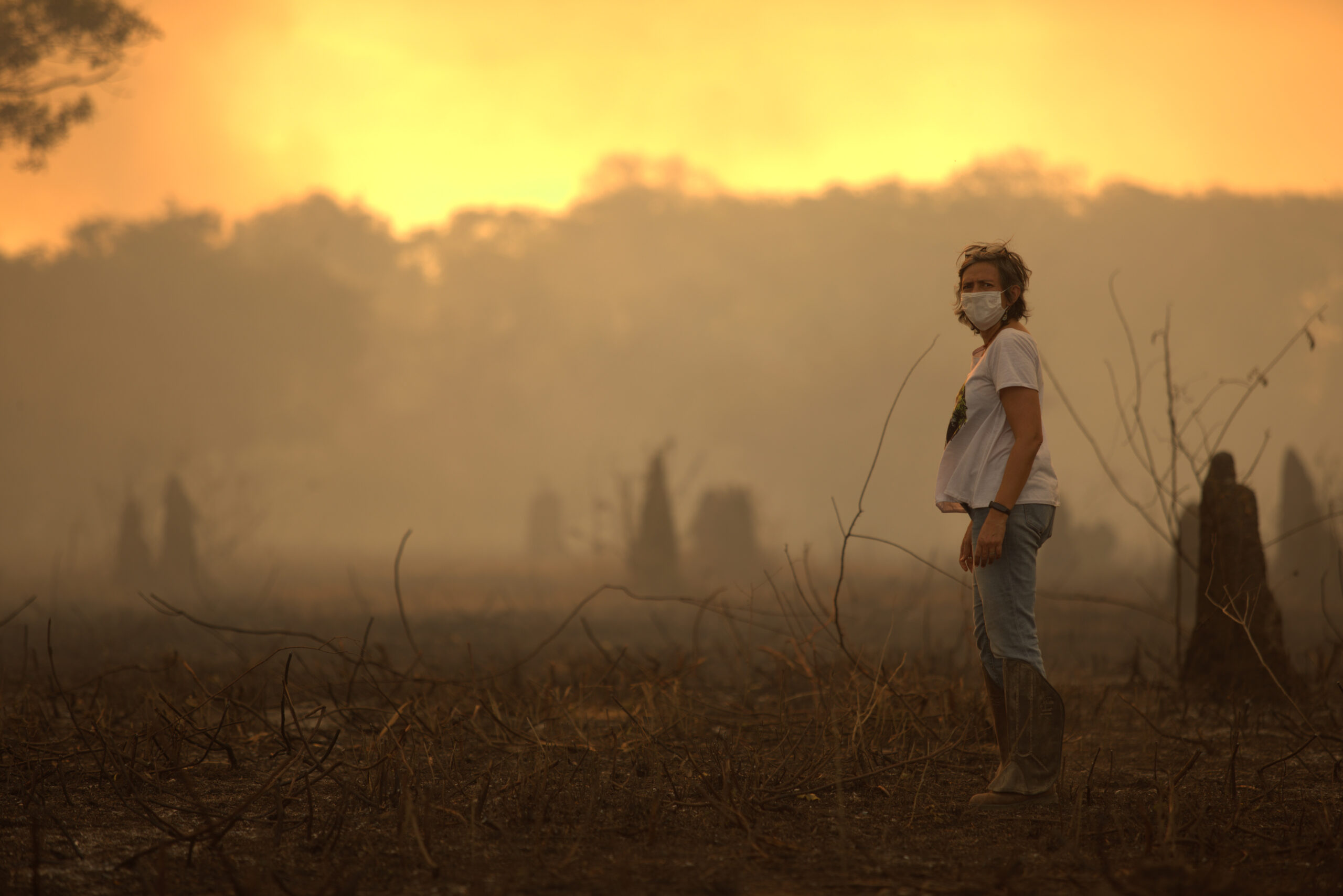 A researcher wearing a mask stands in a smoky, orange-lit landscape