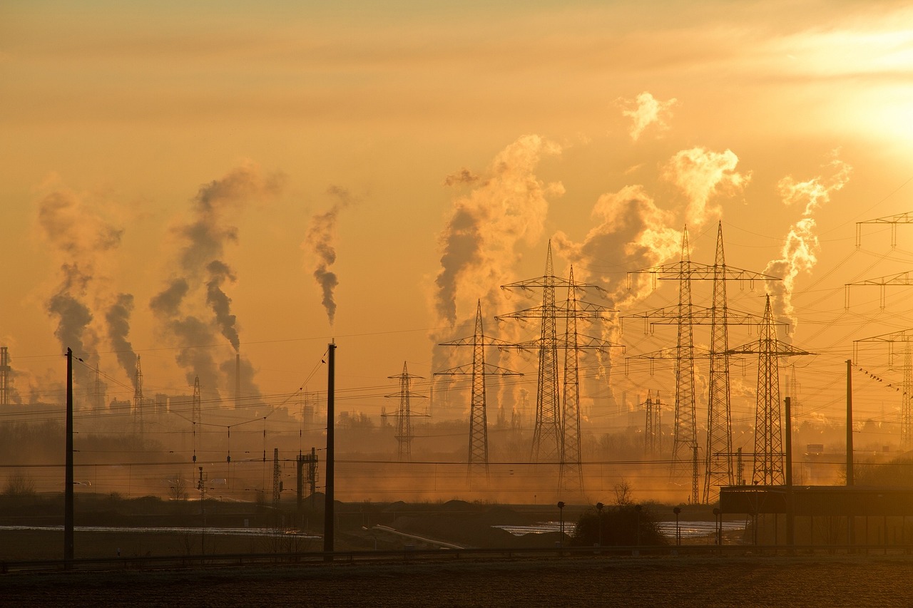 Smokestacks release plumes of exhaust into an orange sky