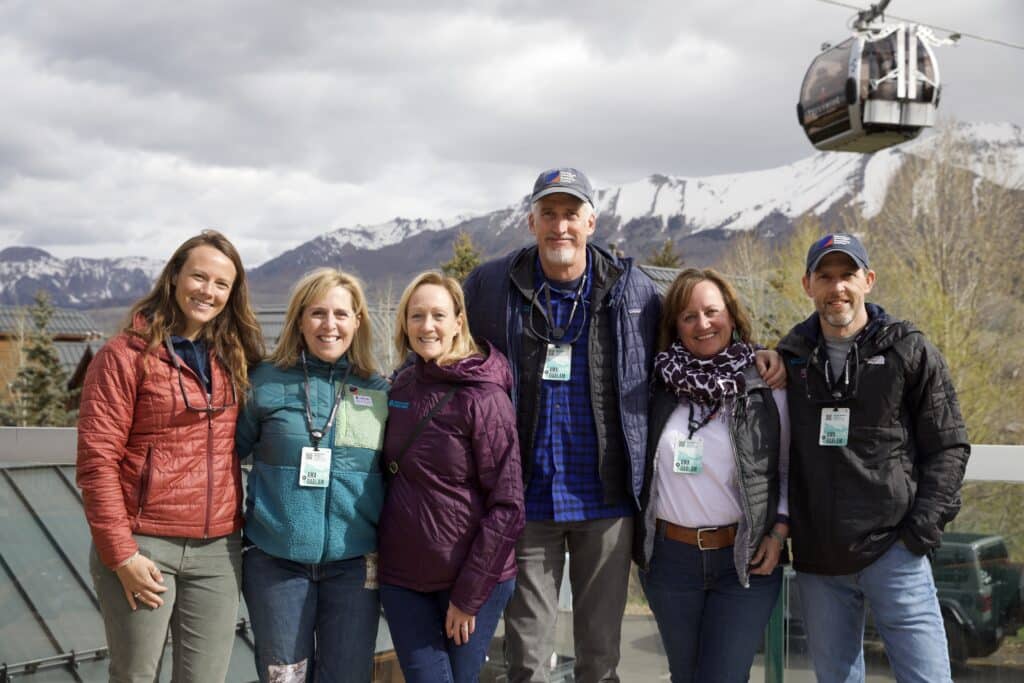 Alli Cunningham, Nancy Bridges, Leslie Kolterman, R. Max Holmes, Corrie Martin, and Wayne Walker pose for a picture with mountains and a cable car in the background