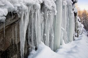 a bunch of thick icicles hanging from a snowy rock edge