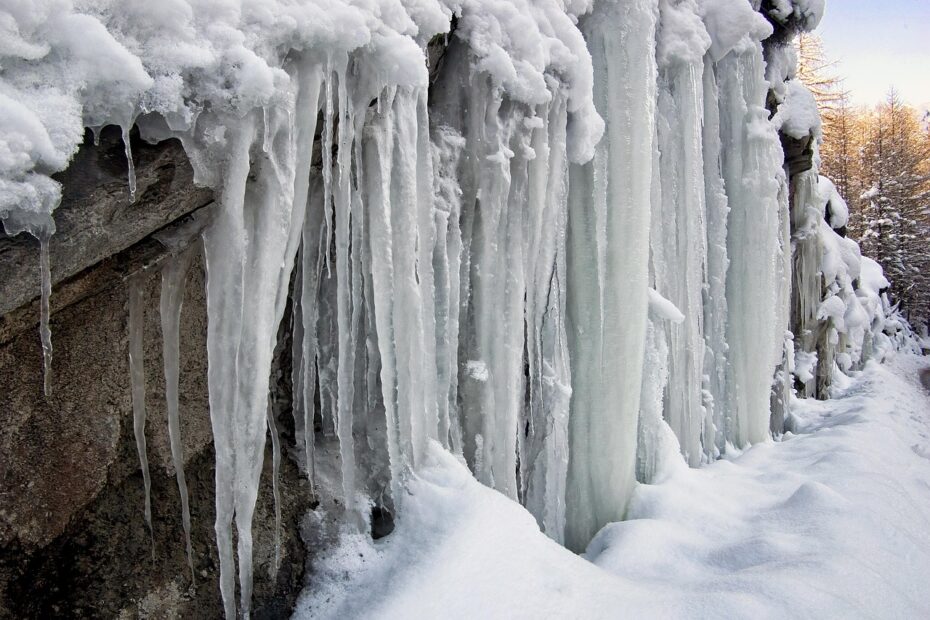 a bunch of thick icicles hanging from a snowy rock edge
