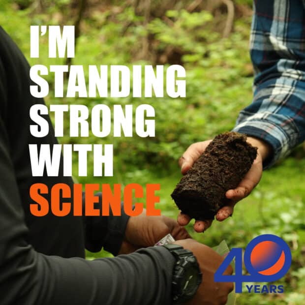 one hand holding a dark brown cylindrical soil sample, putting it into a bag held by someone else. overlaid on the photo is the text "I'm standing strong with science"