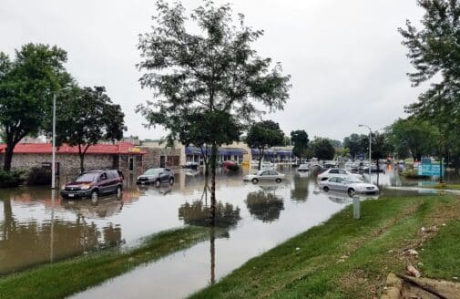 cars in the flooded parking lot of a strip mall, with water reaching about halfway up their tires