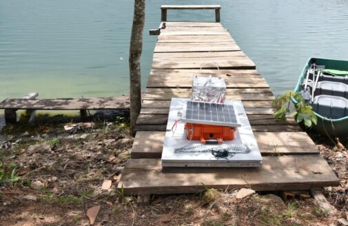 a floating methane chamber sits on a dock by a lake, next to a small green boat