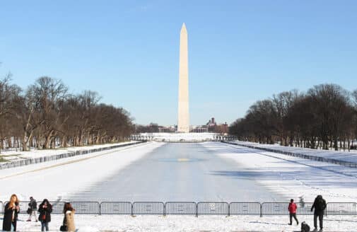 snow covers the national mall looking down the reflecting pool towards the washington monument