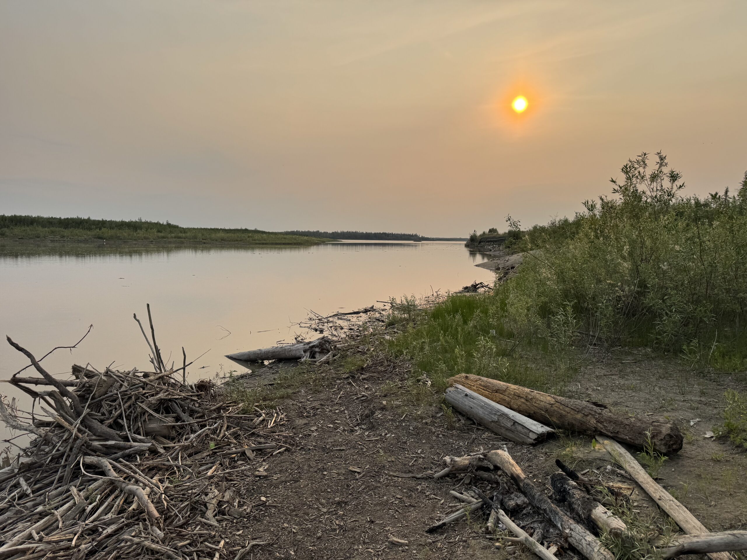 orange sun in a hazy sky over a river near yukon flats alaska