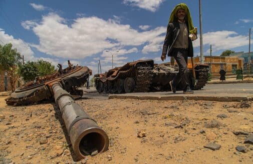 a man passes by a destroyed tank in the street
