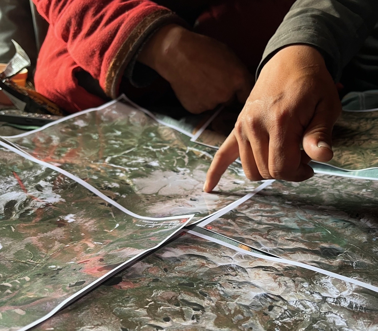 a hand points to something on a set of printed maps