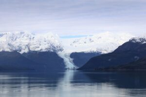 a glacier sits between two slopes, with a fjord in the foreground