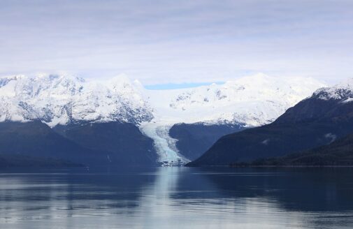 a glacier sits between two slopes, with a fjord in the foreground