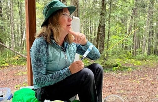 kathleen savage sits in a forest holding a syringe containing a water sample