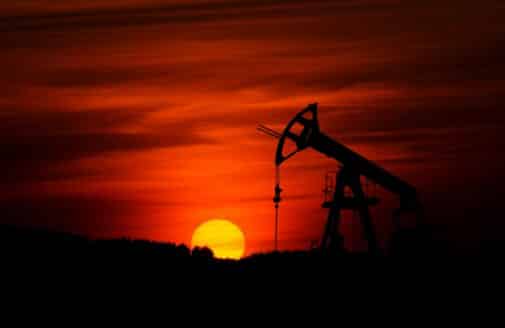 a pump jack mines crude oil, backlit by a deep red sunset