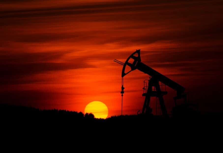 a pump jack mines crude oil, backlit by a deep red sunset