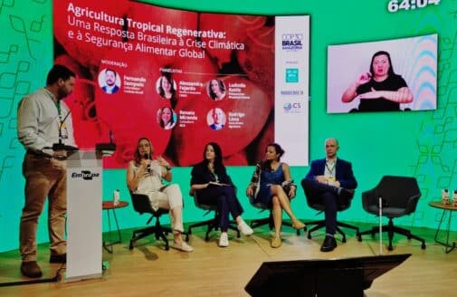 Ludmila Rattis sits on a panel, speaking into a microphone while the others on the panel, and the moderator behind the podium, look at her and listen