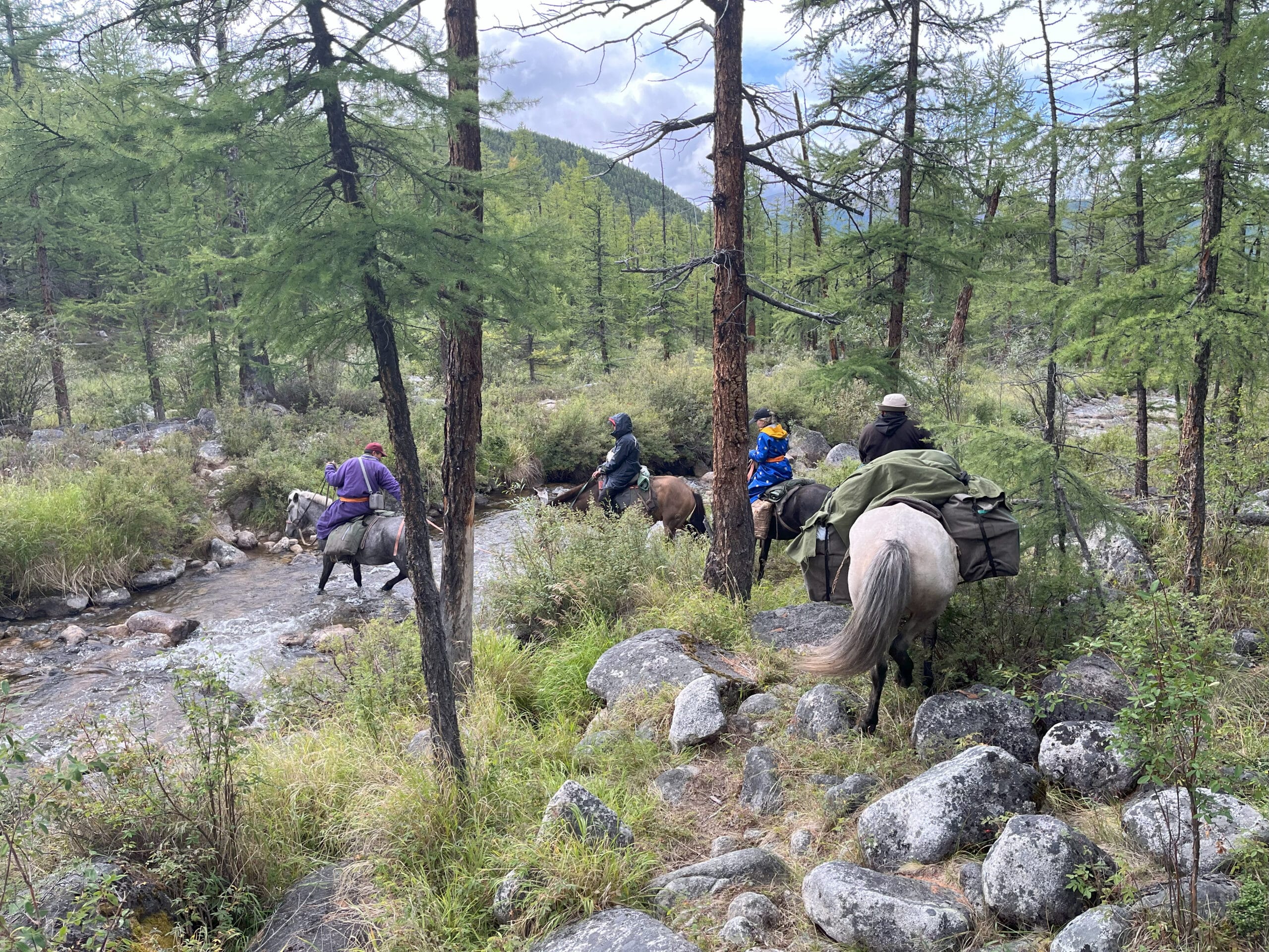 A line of horseback riders crossing a small stream
