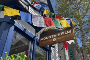a wooden sign reading "mountainfilm" hangs in front of some windows, amongst colorful tibetan prayer flags