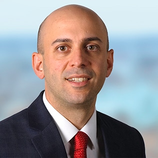 headshot of Chris Goolgasian, wearing a black suit jacket, white collared shirt, and red tie