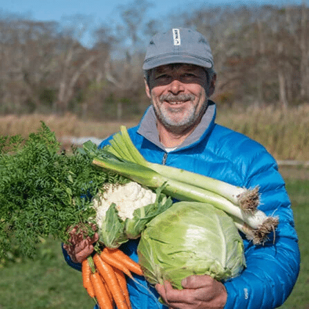 photo of Andrew Woodruff holding a bunch of carrots, a cauliflower, a cabbage, and leeks